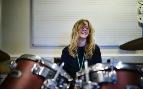student smiling while playing the drums