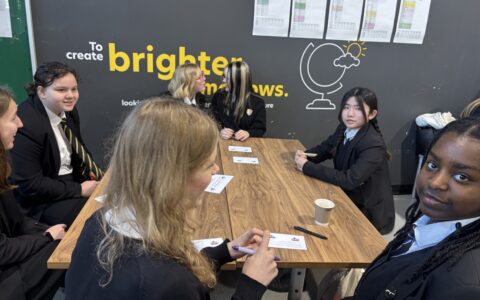 A group of girls sat smiling and laughing whilst enjoying hot chocolate and completing a quiz on paper.